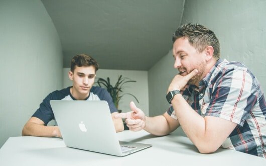 dois homens conversando olhando para um notebook